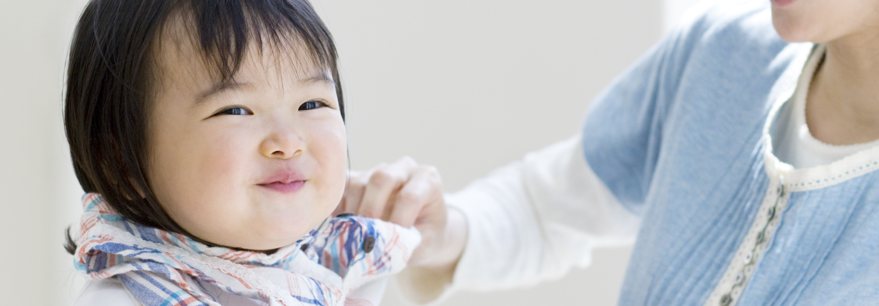 微笑む幼児の襟元を整えている、青い服を着た大人